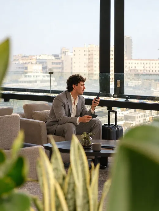 Homem de 45 anos com celular e cartão num lounge com vista da cidade, pronto para viajar